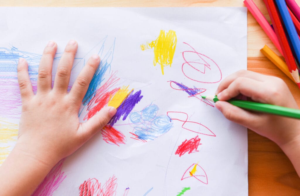 Child's hands coloring with colored pencils on white paper. 